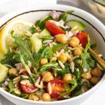 Close-up image of orzo salad in a bowl with a lemon wedge on top.