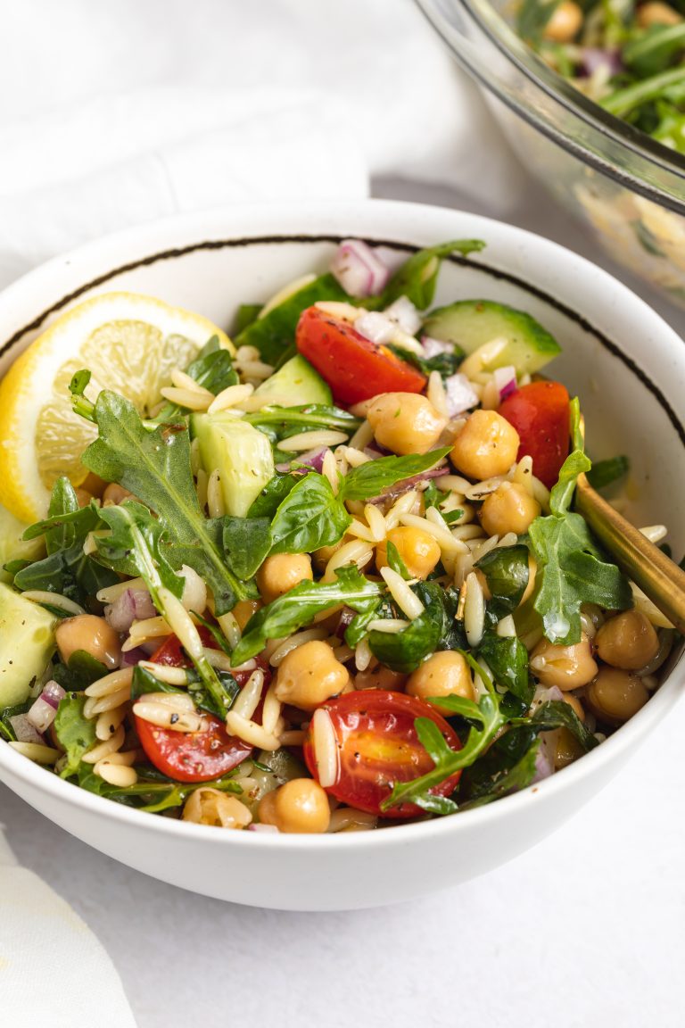 Close-up image of orzo salad in a bowl with a lemon wedge on top.