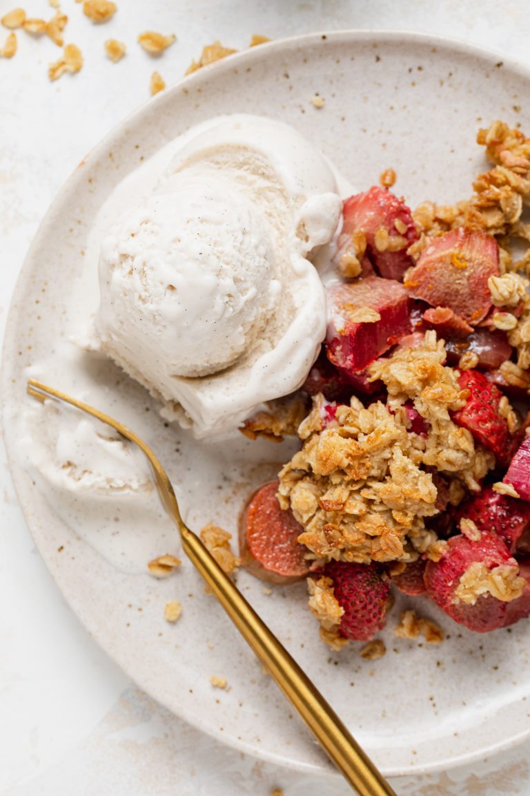 strawberry rhubarb crisp on a plate with a scoop of vanilla ice cream
