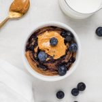 overhead image of peanut butter and jelly baked oats with milk and blueberries on the side.