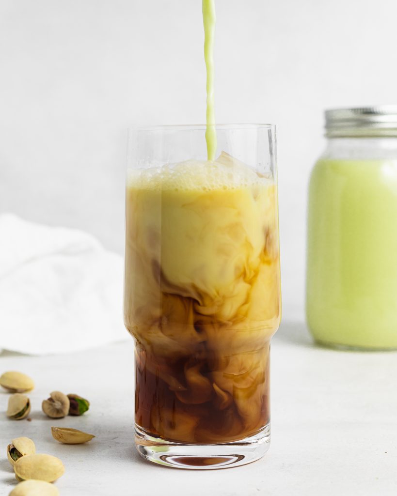 pistachio milk being poured into a glass of iced coffee
