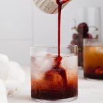 cherry cordial being poured into a glass of ice and sparkling water