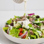 tzatziki dressing being poured over a gyro salad