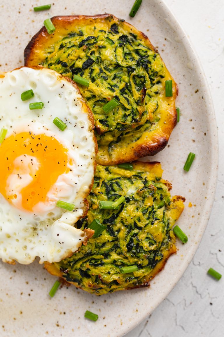 two zucchini hash browns on a plate with a fried egg on top