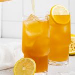 lemonade being poured into a glass of an arnold palmer drink with lemon slices on the side