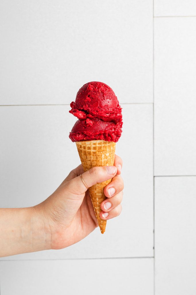hand holding a cone of vegan raspberry sorbet