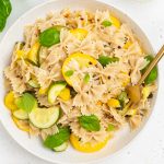 summer squash pasta on a plate with white wine, basil, and red pepper flakes on the side