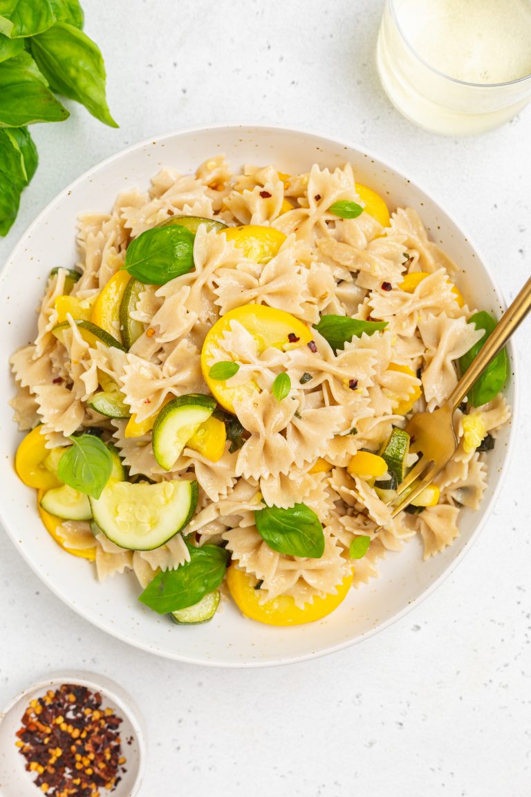 summer squash pasta on a plate with white wine, basil, and red pepper flakes on the side