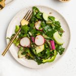 swiss chard salad on a plate with a fork and sunflower seeds on the side