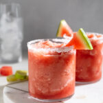 frozen watermelon margaritas in two glasses with a watermelon slice on the rim.