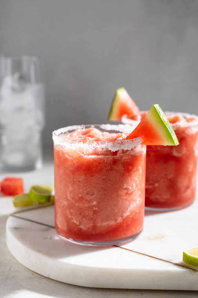frozen watermelon margaritas in two glasses with a watermelon slice on the rim.