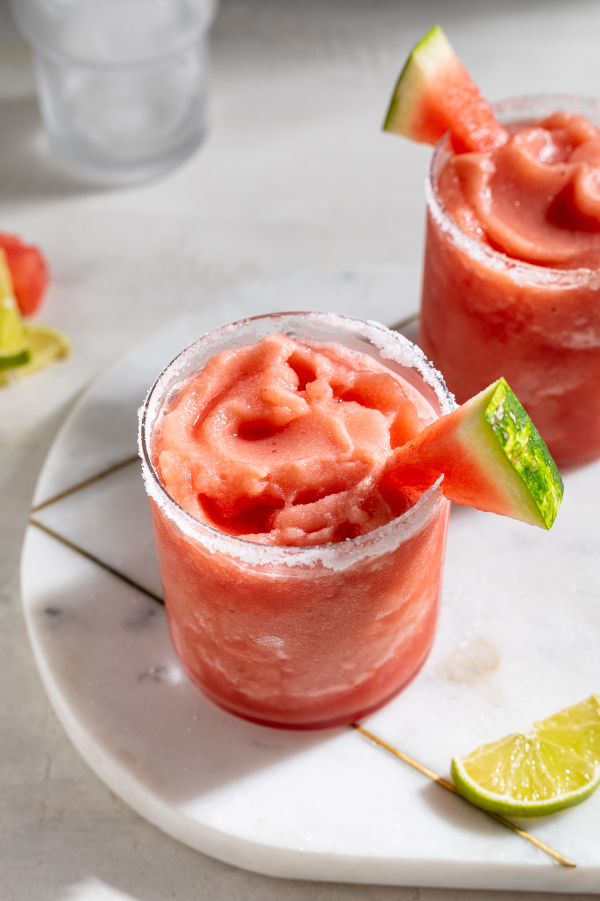 two frozen watermelon margaritas with limes on the side.