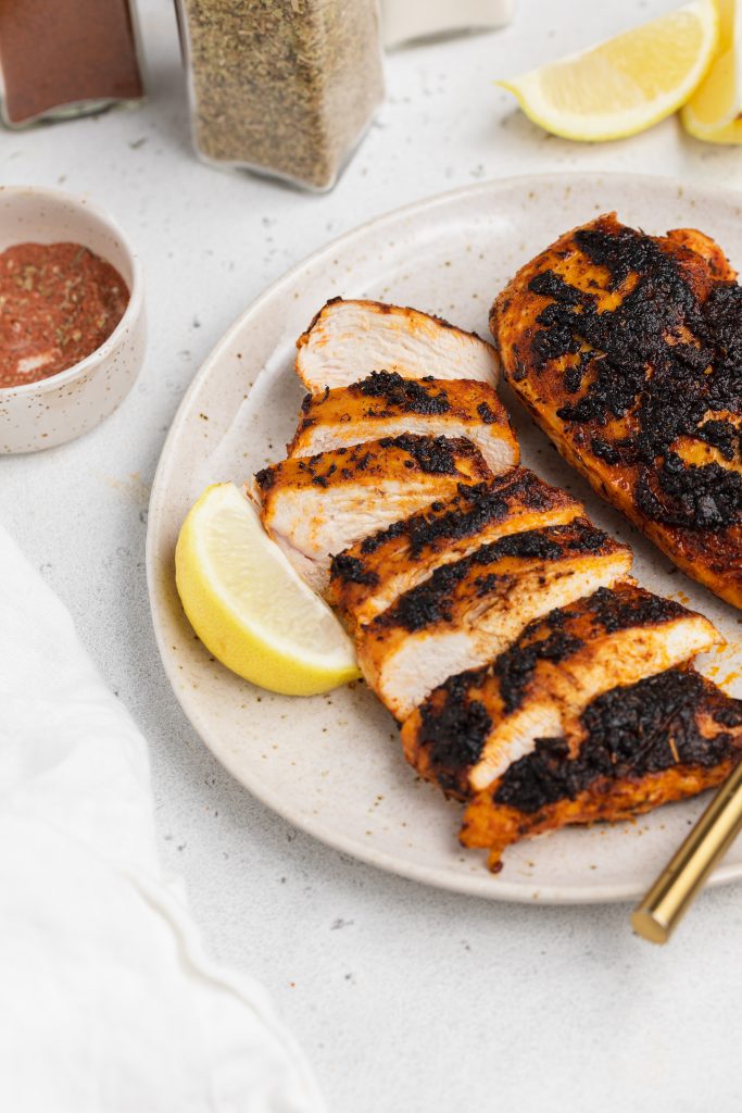 blackened chicken on a plate with lemon wedges on the side and blackened seasoning on the side