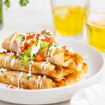 chicken taquitos on a plate with two glasses of beer and cilantro on the side