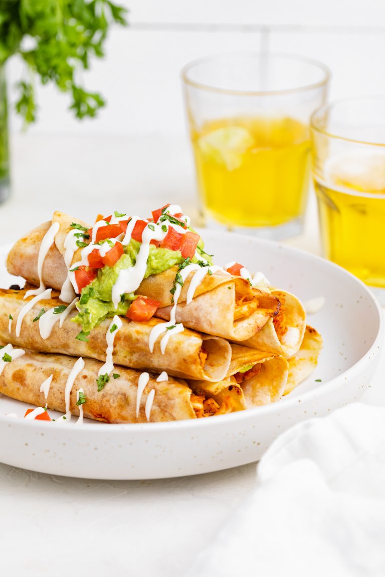 chicken taquitos on a plate with two glasses of beer and cilantro on the side