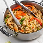 pork stir fry in a pan with tongs and lime wedges on the side