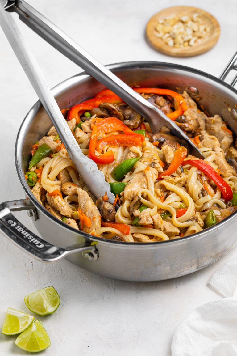 pork stir fry in a pan with tongs and lime wedges on the side