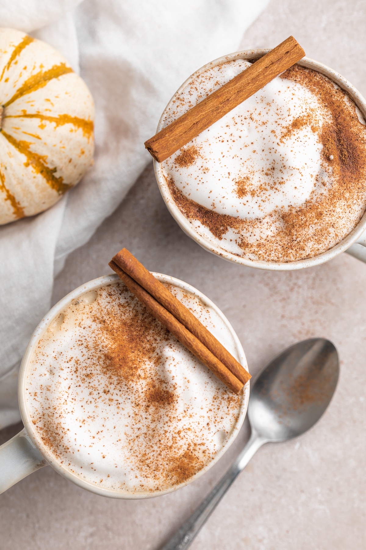 overhead image of two pumpkin spice lattes with cinnamon sticks on top.