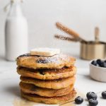 stacked almond flour pancakes with blueberries, butter, and powdered sugar on top