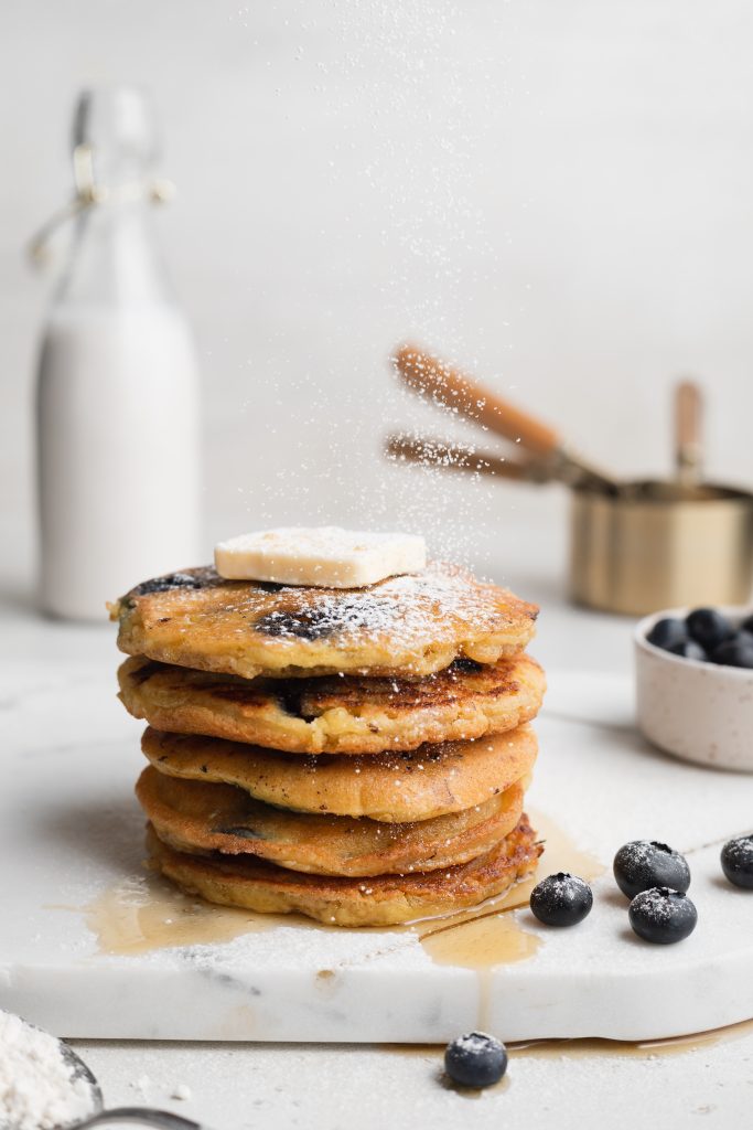 stacked almond flour pancakes with blueberries, butter, and powdered sugar on top