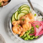 close-up overhead image of bang bang shrimp bowl with cucumber, edamame, pickled red onion, and white rice