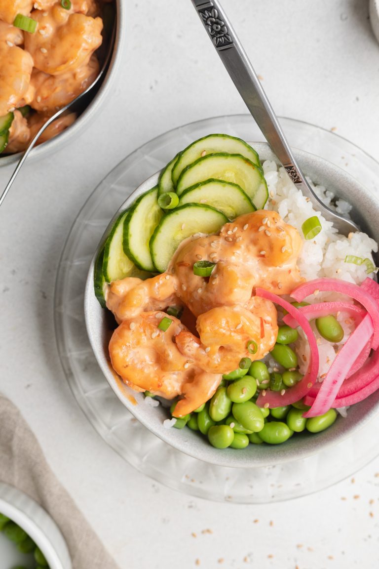 close-up overhead image of bang bang shrimp bowl with cucumber, edamame, pickled red onion, and white rice