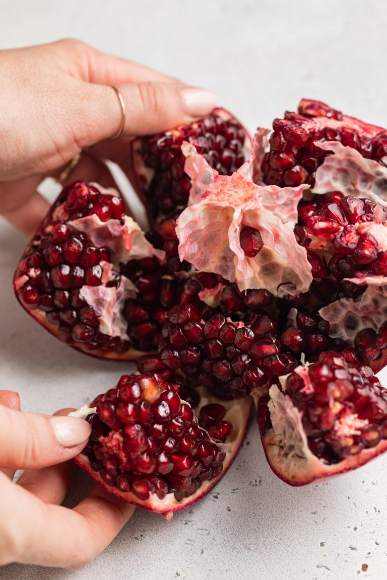 hands opening up a pomegranate and exposing the seeds