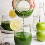 green blender juice being poured into a glass, garnished with a lemon slice