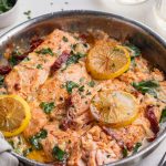 sun dried tomato salmon recipe in a skillet with while wine and fresh parsley on the side