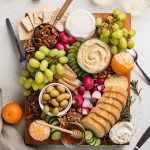 overhead image of the entire vegan charcuterie board with white wine, utensils, and bread on the side