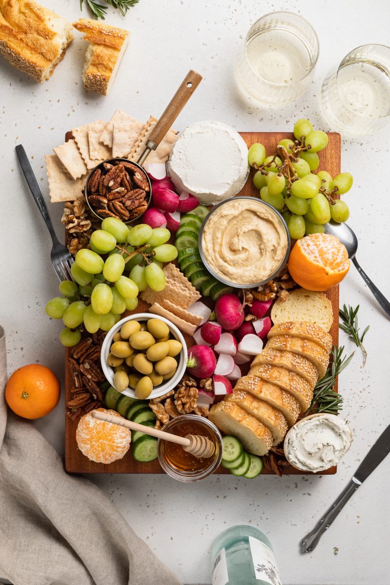 overhead image of the entire vegan charcuterie board with white wine, utensils, and bread on the side