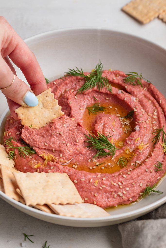 roasted beet hummus being scooped out of a bowl with a cracker
