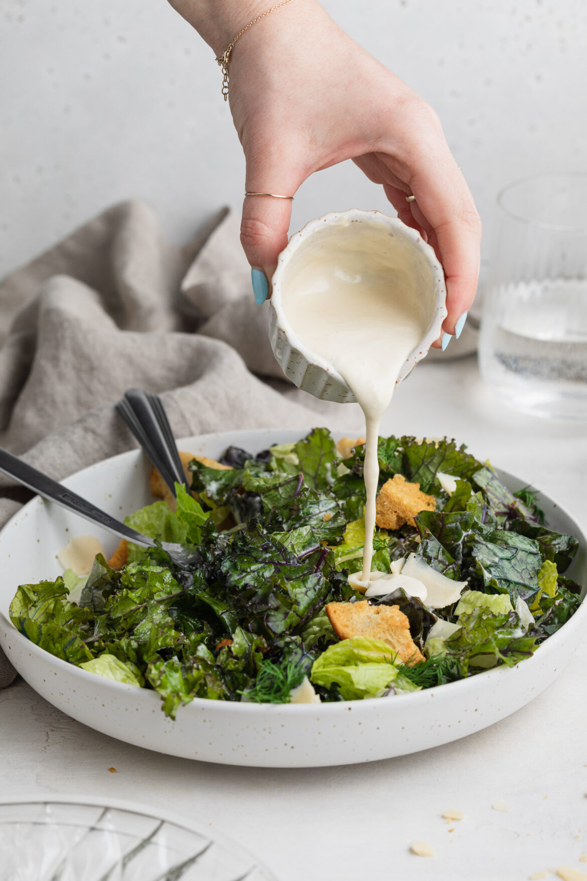Quick and Easy Kale Caesar Salad dressing being poured over kale caesar salad