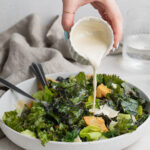 dressing being poured over kale caesar salad