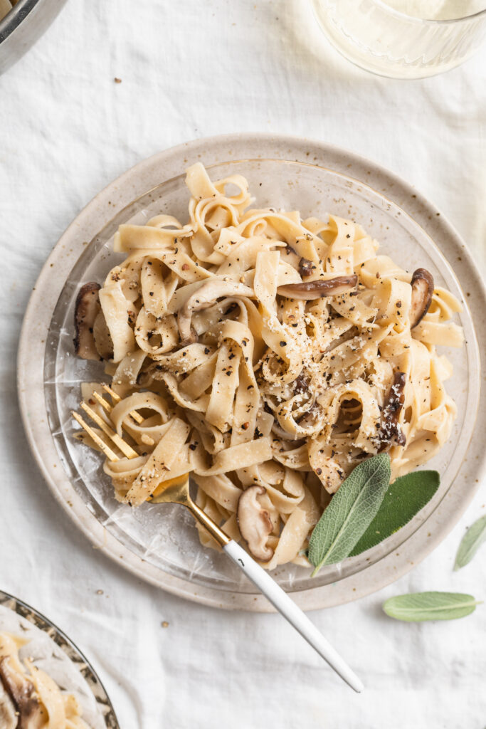 overhead image of mushroom pasta on a plate with white wine on the side