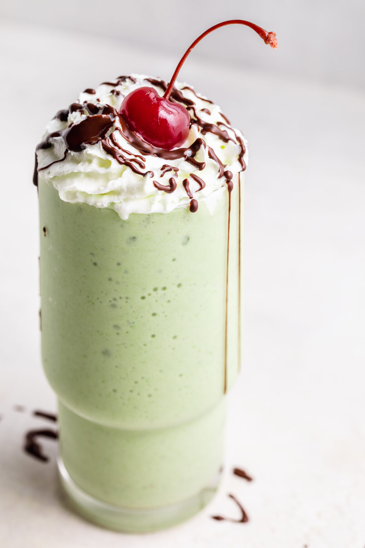 Healthy Shamrock Shake healthy shamrock shake in a glass with whipped cream, melted chocolate, and a cherry on top