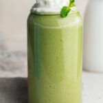 healthy shamrock shake in a glass with whipped cream and fresh mint on top.