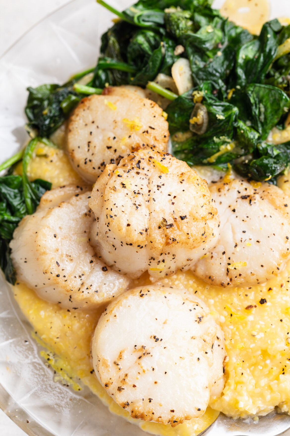 Perfect Seared Scallops Recipe with Garlicky Greens and Polenta close-up image of seared scallops with polenta and garlicky greens on a plate.