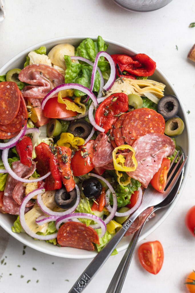 close-up overhead image of antipasto salad on a plate with tomatoes on the side