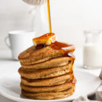 maple syrup being poured over a stack of oat flour pancakes