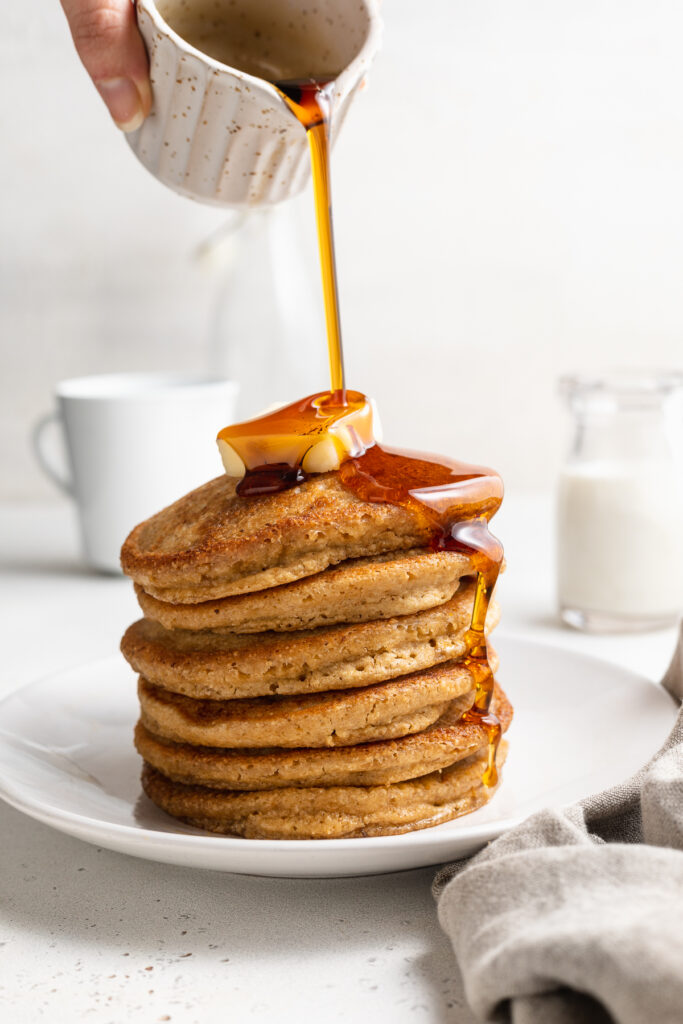 maple syrup being poured over a stack of oat flour pancakes