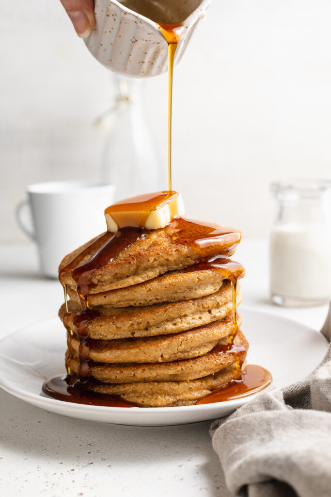 a stack of oat flour pancakes with maple syrup being poured on top