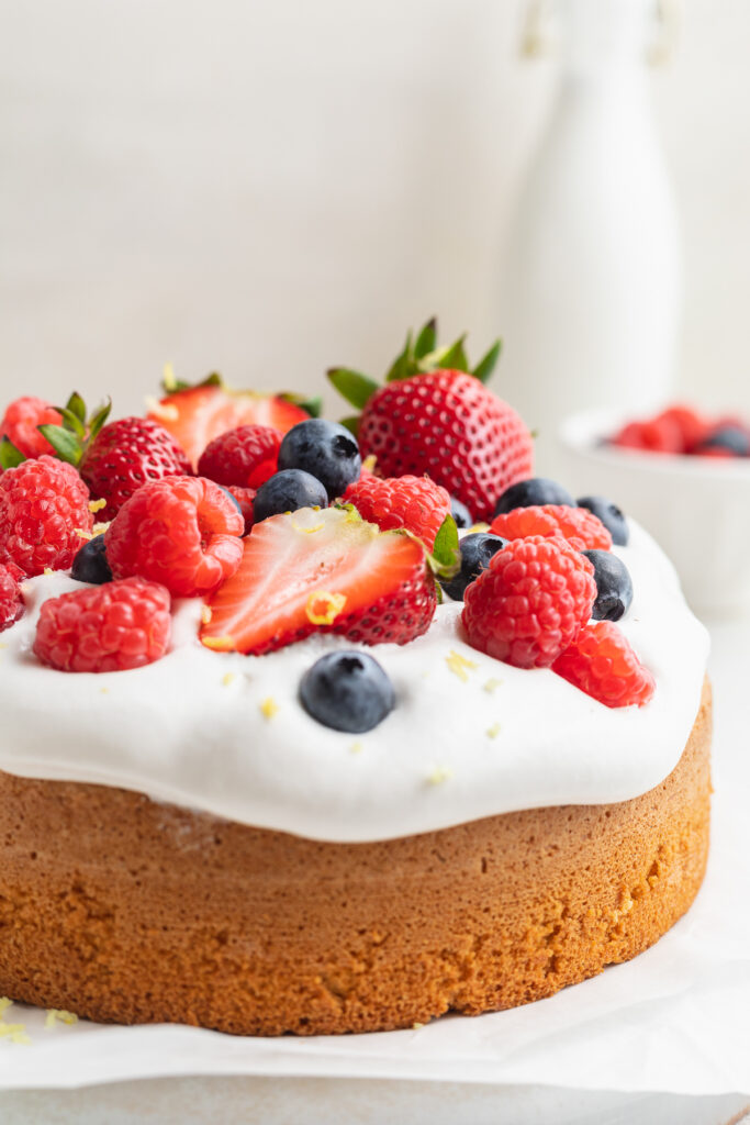 close-up image of almond flour cake with coconut whipped cream and berries on top.