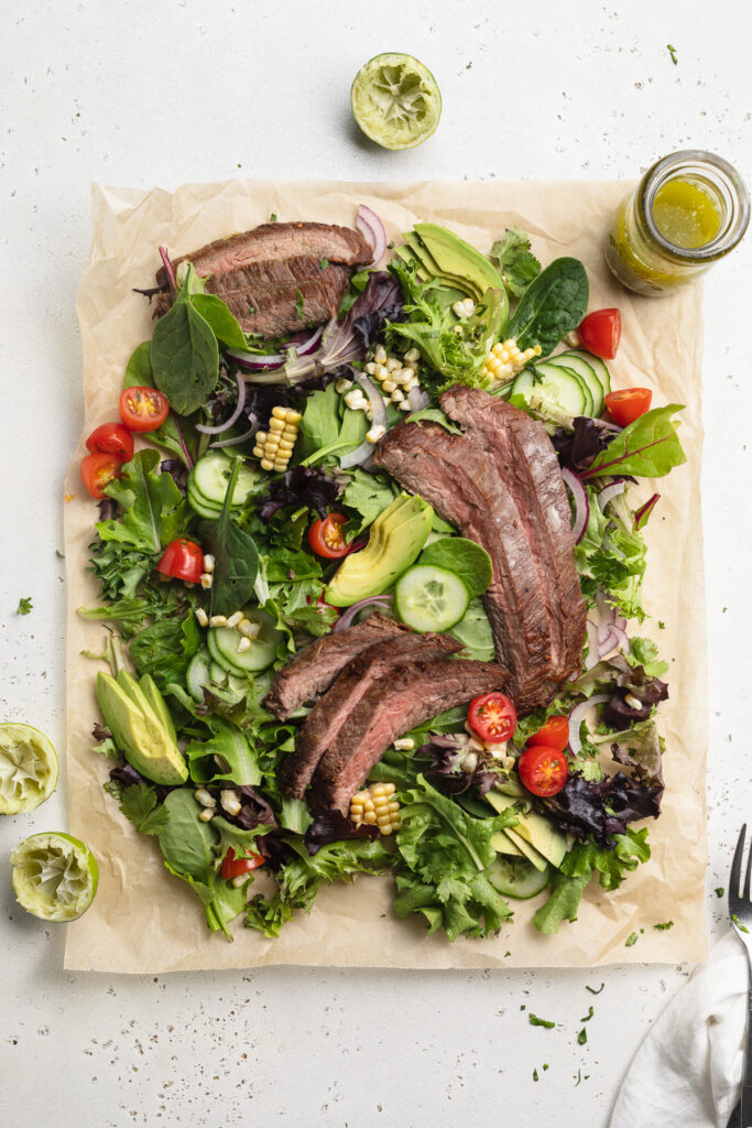 Overhead image of steak salad on parchment paper with cilantro lime dressing on the side.