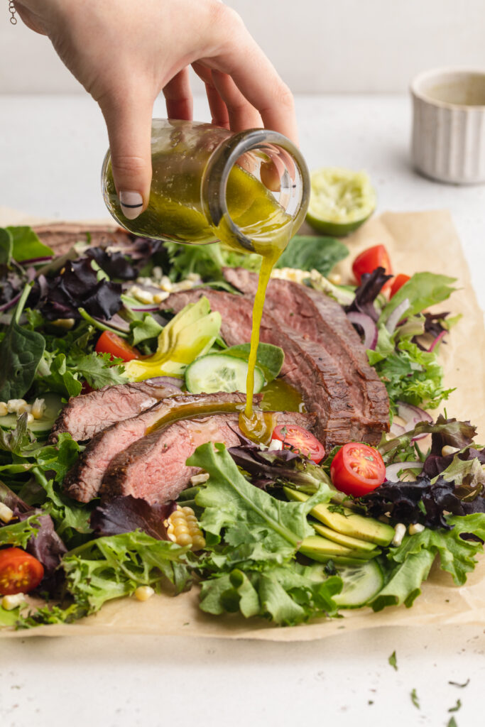 cilantro lime dressing being poured over steak salad.