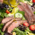 close-up image of dressing being poured over steak salad