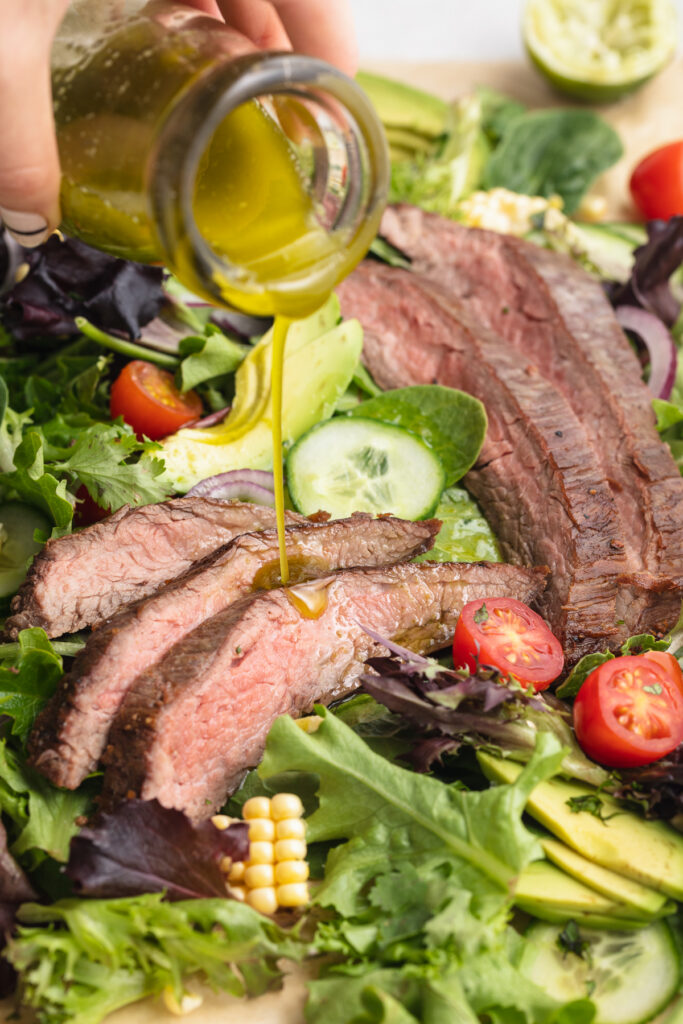 close-up image of dressing being poured over steak salad