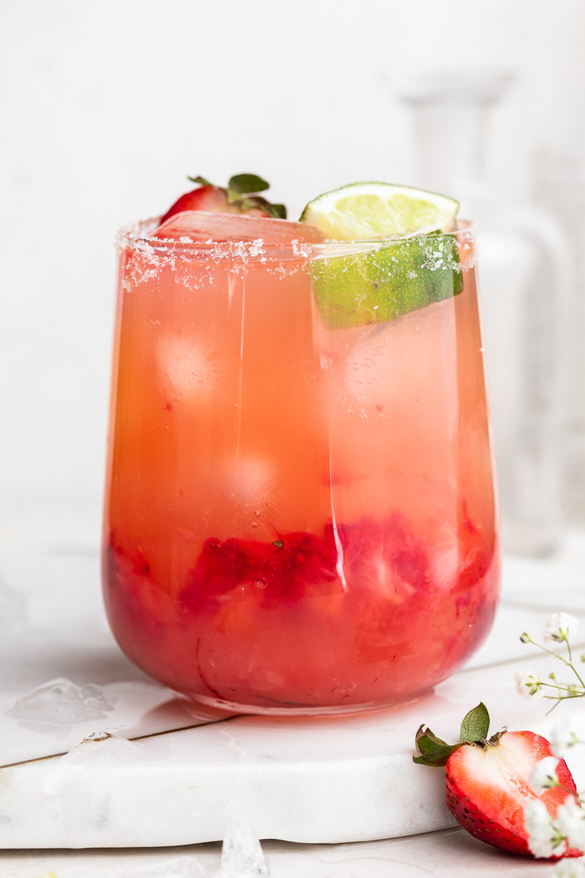 Skinny Strawberry Margarita Recipe close-up image of a skinny strawberry margarita in a glass with fresh strawberries and lime wedges on top.