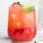 close-up image of a skinny strawberry margarita in a glass with fresh strawberries and lime wedges on top.