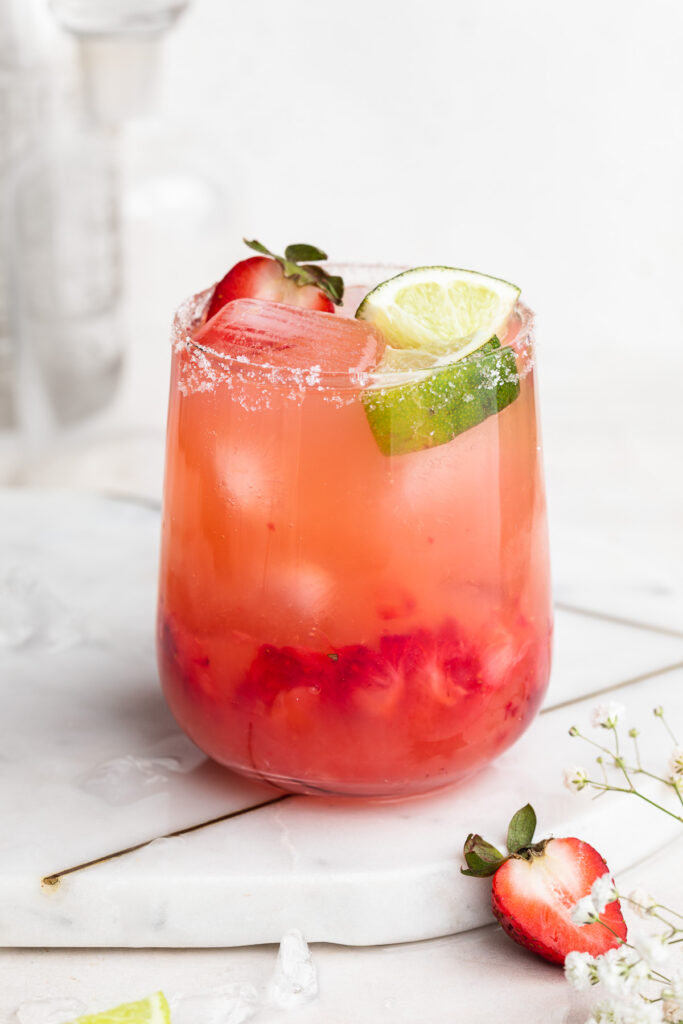skinny strawberry margarita in a glass with fresh strawberries and lime wedges on top.